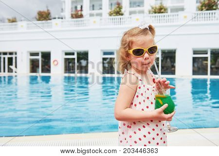 Cute little blonde at the pool and holding achild's cocktail .