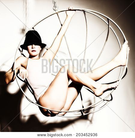 sexy woman in a beige swimsuit and black hat on a metal cage on a white background.