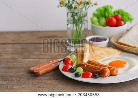 Homemade breakfast with sunny side up fried egg toast sausage fruits vegetable strawberry jam and orange juice in side view with copy space. Delicious homemade american breakfast concept for background. American breakfast with copy space.