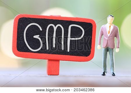Businessman stand near wooden sign of GMP Text in Concept of quality management system.