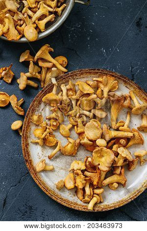 Heap of fresh uncooked forest mushrooms chanterelle in old pan over dark gray texture background. Top view with space