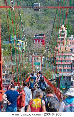 Rishikesh, India - March 10, 2017: People Crossing The Ganges River On The Suspension Footbridge At