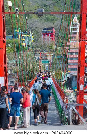 Rishikesh, India - March 10, 2017: People Crossing The Ganges River On The Suspension Footbridge At