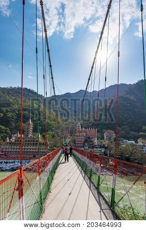 Rishikesh, India - March 10, 2017: People Crossing The Ganges River On The Suspension Footbridge At