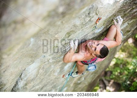 Young male rock climber on challenging route gripping small handholds. View from above.