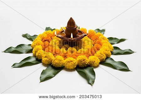 flower rangoli for Diwali or pongal or onam made using marigold or zendu flowers and red rose petals over white background with diwali diya in the middle, selective focus