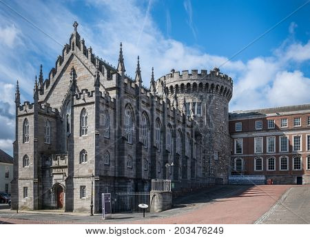 Dublin Ireland - August 7 2017: Original church and tower of The Castle build with dark gray stones under blue sky with white clouds. Newer side building in back.