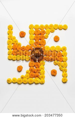 stock photo of hindu auspicious symbol called Swastika or swastik made using marigold flower/zendu/genda phool & diwali diya / clay lamp, Flower rangoli in the shape of Swastika for diwali/pongal/onam