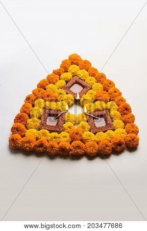 flower rangoli for Diwali or pongal or onam made using marigold or zendu flowers and red rose petals over white background with diwali diya in the middle, selective focus