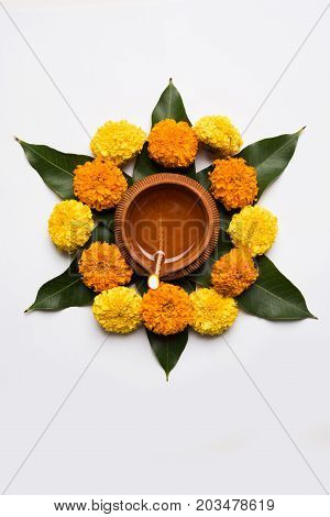 flower rangoli for Diwali or pongal or onam made using marigold or zendu flowers and red rose petals over white background with diwali diya in the middle, selective focus
