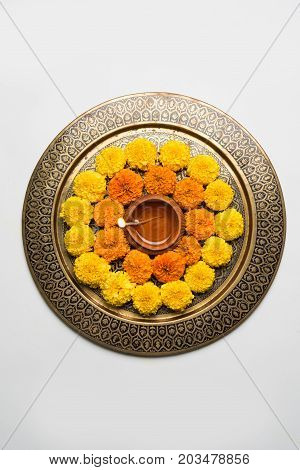 flower rangoli for Diwali or pongal or onam made using marigold or zendu flowers and red rose petals over white background with diwali diya in the middle, selective focus