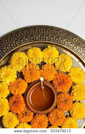 flower rangoli for Diwali or pongal or onam made using marigold or zendu flowers and red rose petals over white background with diwali diya in the middle, selective focus