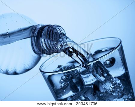pouring water from a plastic bottle into a glass with ice on a light blue background