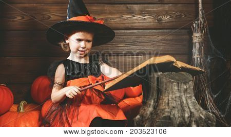 Halloween. little witch child conjures with book of spells magic wand and pumpkins