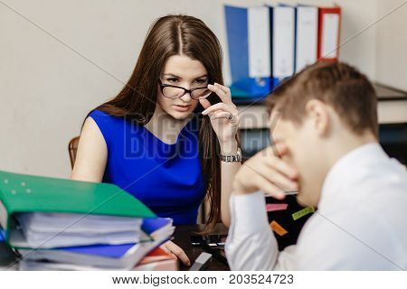 Young Beautiful Girl In Glasses And A Blue Dress Is Sitting In The Office And Trying To Catch A Lie