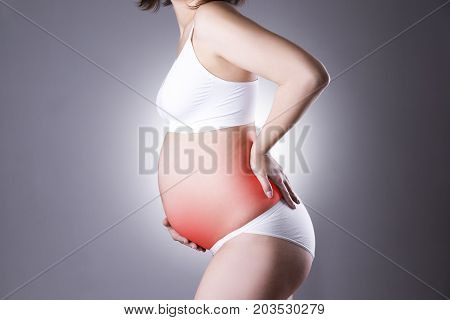 Caucasian pregnant woman in white lingerie with back and abdominal pain on gray studio background. Pregnancy concept