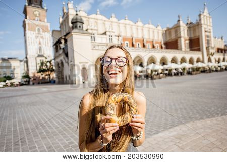 Young woman tourist eating prezel on the market square in Krakow in Poland