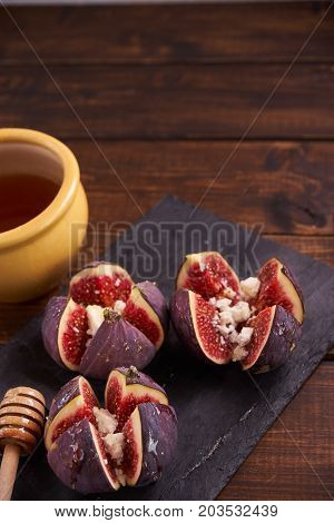 Vertical shot of three figs filled with cheese and honey in a white plate on wooden table. Copy space.