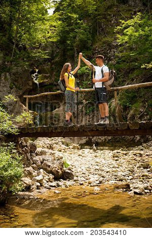Active Young Cople Hiking On A Wooden Brifge Over Mountain Creek