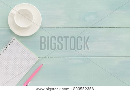 Open notebook with pink pen and coffeecup on mint wooden background. Copy space background top view flat lay overhead