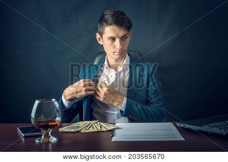 Man Businessman In Suit Puts Money In His Pocket. A Bribe In The Form Of Dollar Bills. Concept Of Co