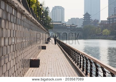 Chengdu, Sichuan Province, China - March 27, 2017: Man walking with arms up by the Jinjiang river with Anshun bridge in the background.