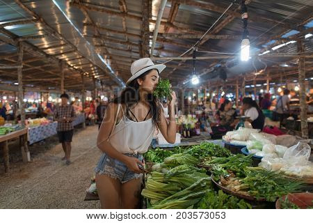 Young Woman Smell Herbs Choosing Green Potherbs On Market Girl Shopping On Traditional Street Bazaar