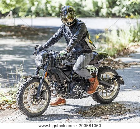 Cool looking motorcycle rider on custom made scrambler style cafe racer in the park