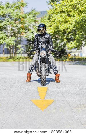Cool looking motorcycle rider on custom made scrambler style cafe racer on the road with an arrow sign