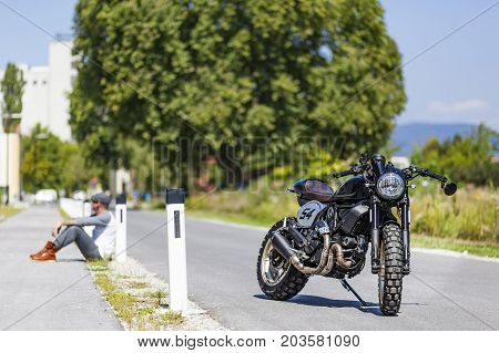 Cool looking motorcycle rider sitting near custom made scrambler style cafe racer
