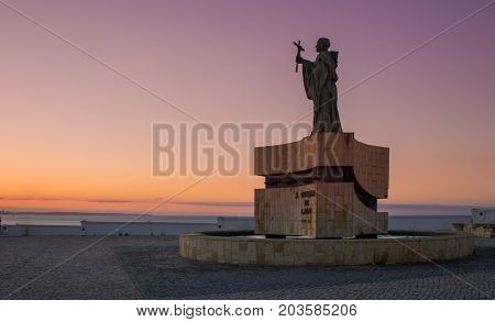 The statue of Saint Goncalo patron of mariners near Atlantic ocean. Sunrise picture with violet light from sun rising. Saint Goncalo with cross blessing to sailors during oversea discoveries.