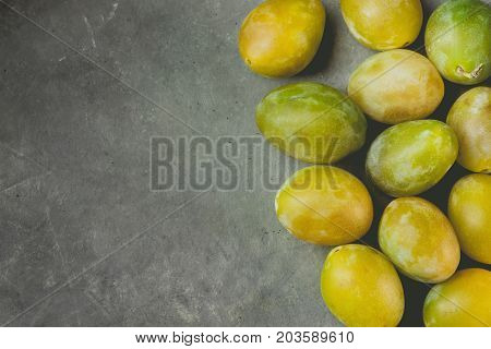 Bunch of scattered ripe juicy yellow and green plums arranged in border on dark stone background. Autumn fall harvest Thanksgiving. Poster template copy space for text. Vintage toning.