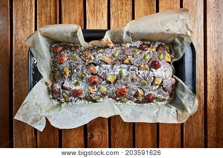 Fresh Homemade Chocolate Brownie Cake With Nuts, Bananas, Coconut And Sugar Powder  On A Wooden Back