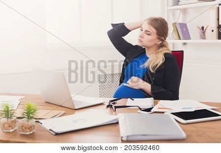 Tired pregnant businesswoman at office copy space. Expectant business lady feeling sick at work, gestosis concept