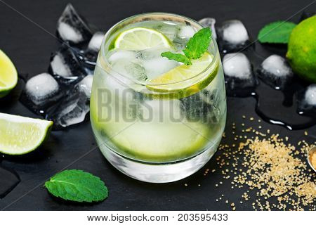 Refreshing mint cocktail mojito with rum and lime, cold drink or beverage with ice on black background, top view