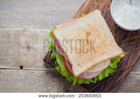Close-up Big Sandwich With Ham, Cheese, Tomatoes, Salad And White Sauce On Toasted Bread On A Rustic