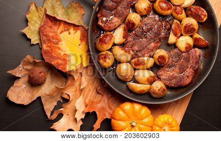 Roast beef steak with roasted potatos in copper pan on wooden table top view. Autumn mood