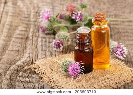 burdock oil in glass bottle and burdock flowers on an old wooden background.