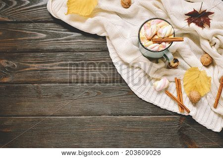 Autumn frame made of dried fall leaves, mug of cocoa with marshmellows, nuts, cinnamon, plaid, apples. Top view on brown wood background. flat lay, copy space