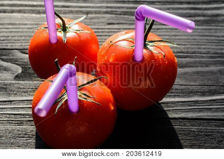 Three Ripe Red Tomatoes with Straws on Black Wooden Table Close-up. Fresh Juice Healthy Food Concept. Tomato as a Vessel with Fresh Juice