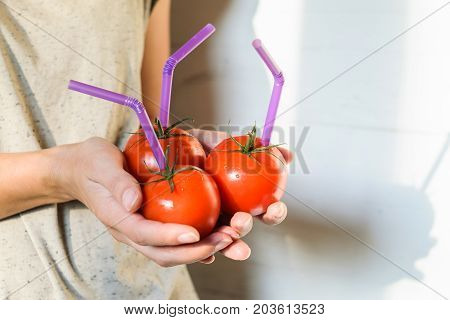 Three Ripe Red Tomatoes with Straws in Woman Hands on Bright Background. Fresh Juice Healthy Food Concept. Tomato as a Vessel with Fresh Juice