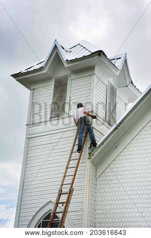 Young man balances on a ladder leaning against a church in Northern Arkansas. He is in the process of helping to reroof an old church.