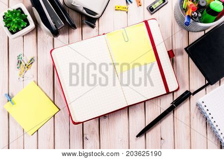 Top view workspace mockup on wooden background with blank notebook with copy space, pen, tacker, punch, clips and accessories. Overhead view. Flat lay, top view