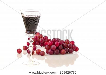 Glass of red wine and red grapes on white taable.