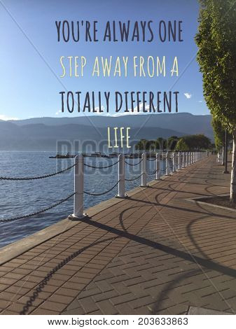 Inspirational motivational text on scenic lake view with brick walkway along lake shore. Conceptual image with words: You're always one step away from a totally different life.