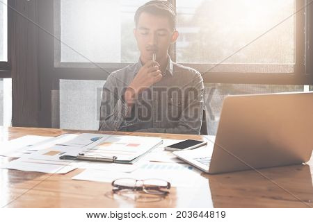 Young asian man working with laptop computer and document while analyzes performance and thinking in office financial investment concept