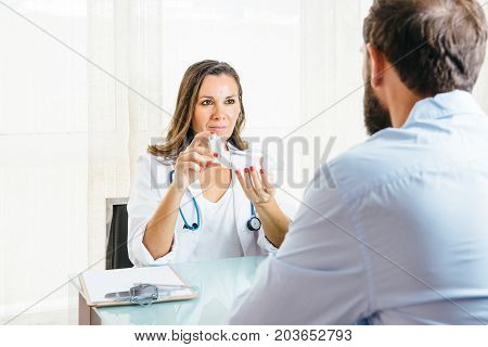 Female doctor explains the use of a an aerosol inhaler placed on a space chamber to a male patient at her office