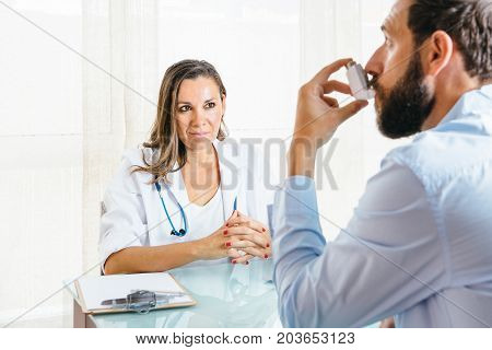 Female doctor looks at a male patient is using an aerosol inhaler at her office