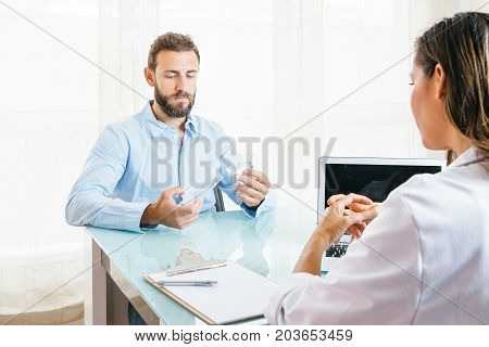 Male patient holds a space chamber and an aerosol inhaler in front of a female doctor at her office