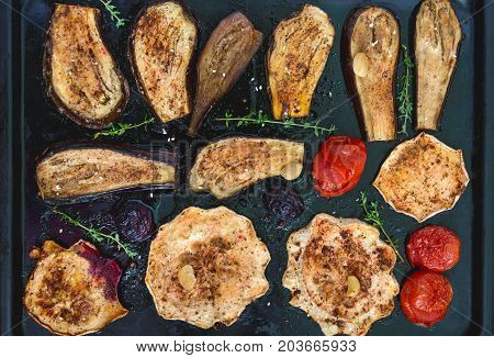 Baked vegetables with herbs and spices: eggplant patisson plums tomatoes on black. Vegetarian cuisine.